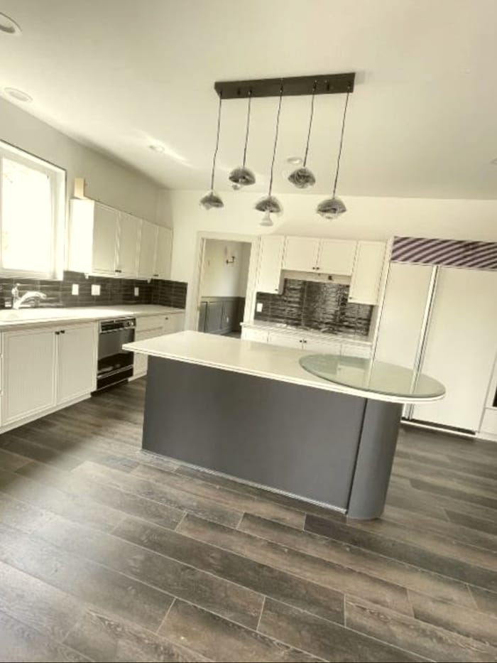 A finished Detroit kitchen after a Mrs. Clean deep clean — bright white cabinets, a dark island, and warm wood floors